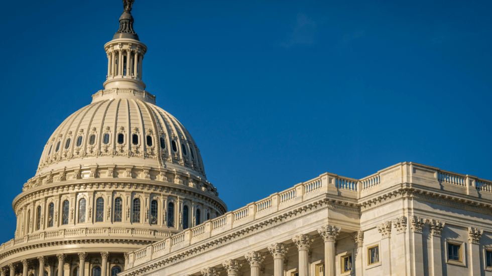The image shows the dome of the United States Capitol building under a clear blue sky.