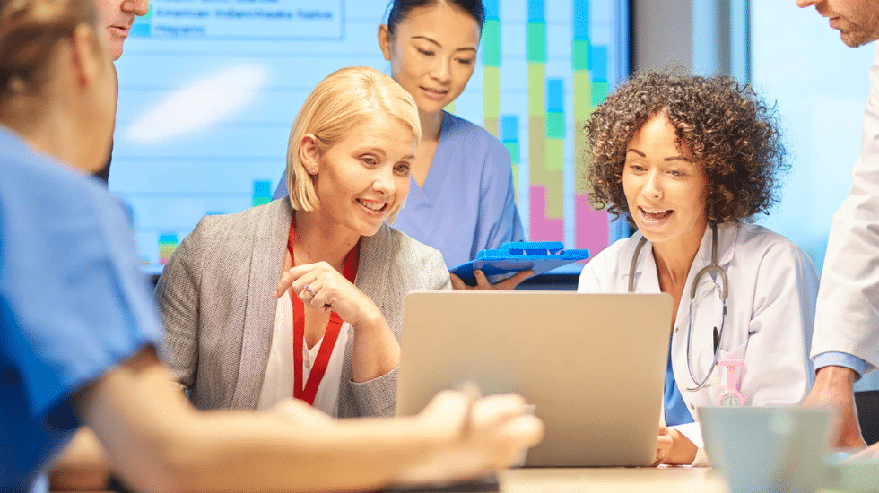 Medical professionals engaged in a collaborative discussion around a laptop, possibly strategizing to improve healthcare services.